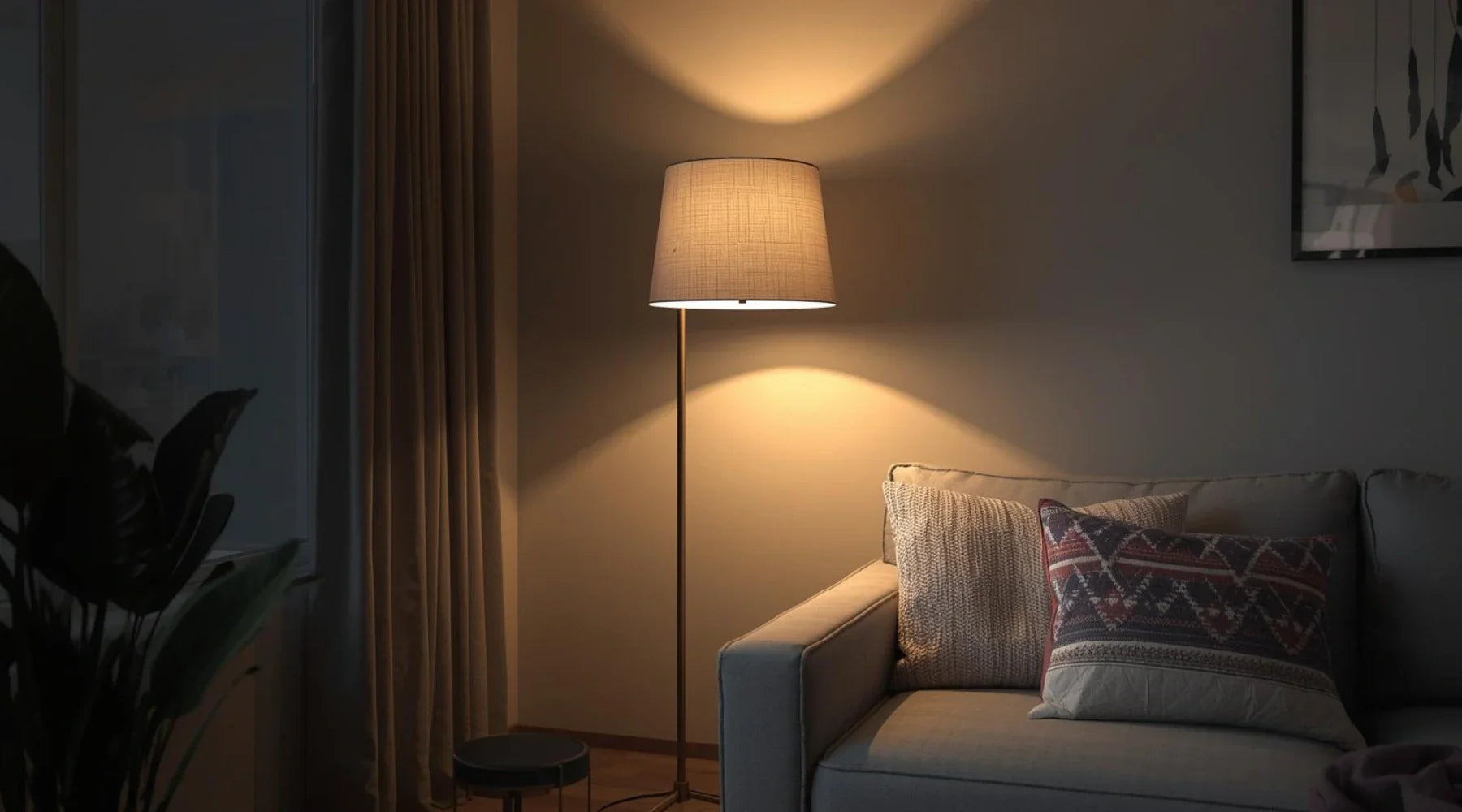 A cozy living room featuring a modern floor lamp, a grey couch with various textured pillows, and soft lighting creating a warm ambiance.