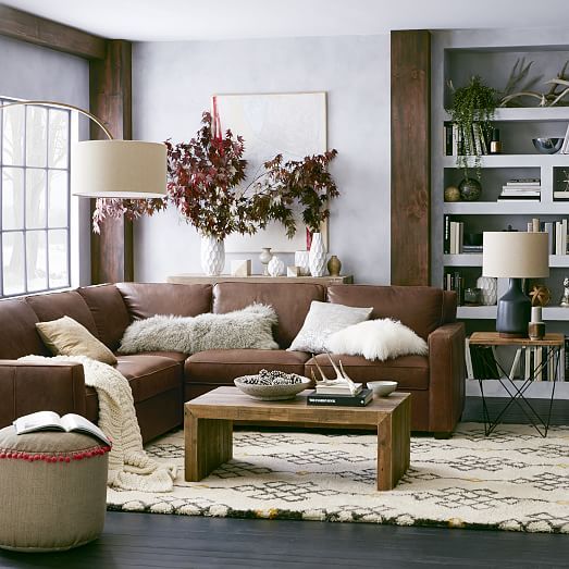 Cozy living room featuring a brown leather sectional, wooden coffee table, decorative plants, and soft textiles in warm tones.