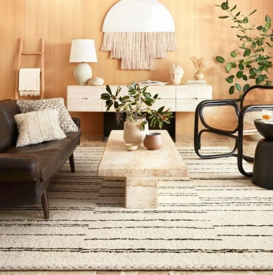 Stylish living room featuring a leather sofa, a marble coffee table, and modern decor with plants and a textured wall hanging.