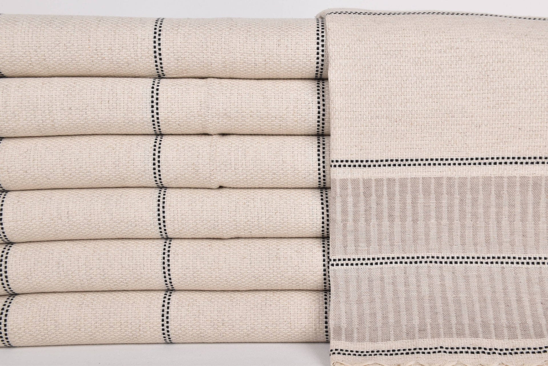 Stack of beige folded towels with black stripes on a light gray background