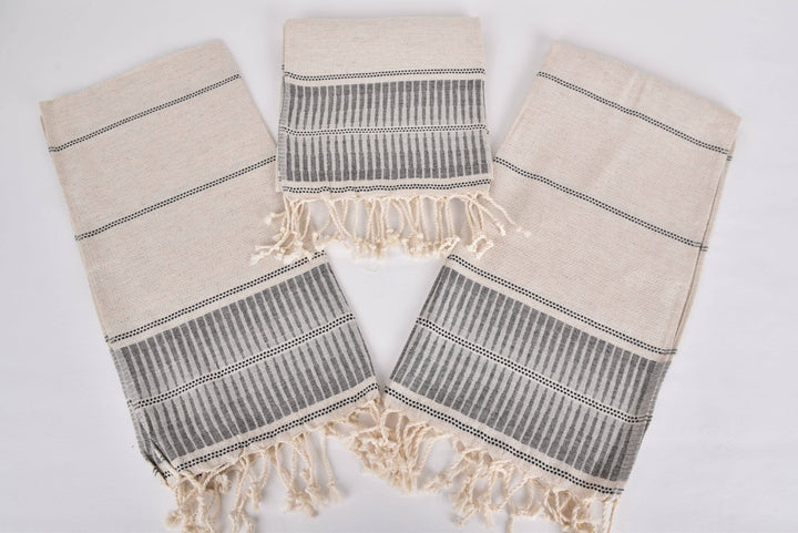 Three beige and gray patterned towels with fringes on a white background