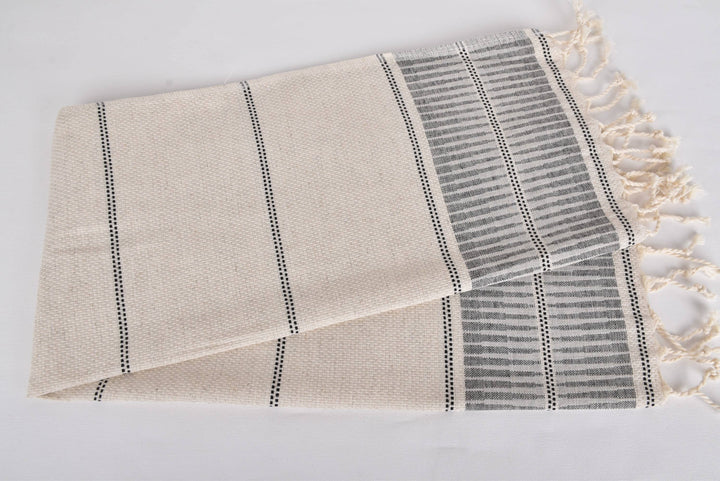 Beige towel with black stripes and tassels on a light gray background