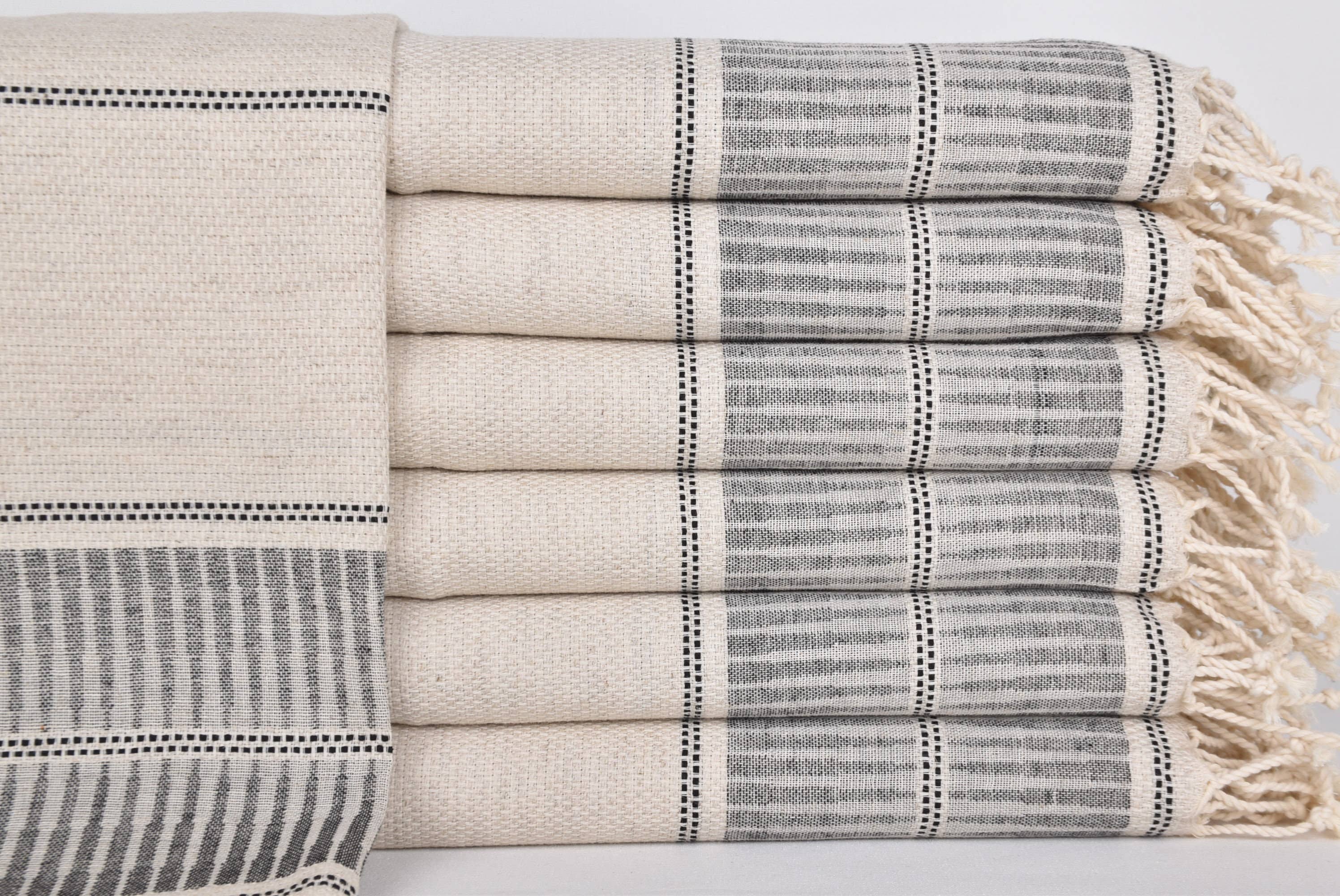 Stack of beige and gray patterned towels with tassels on a light background