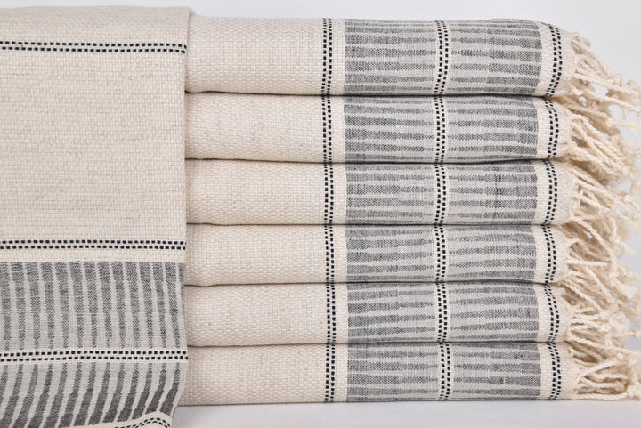 Stack of beige and gray patterned towels with tassels on a light background