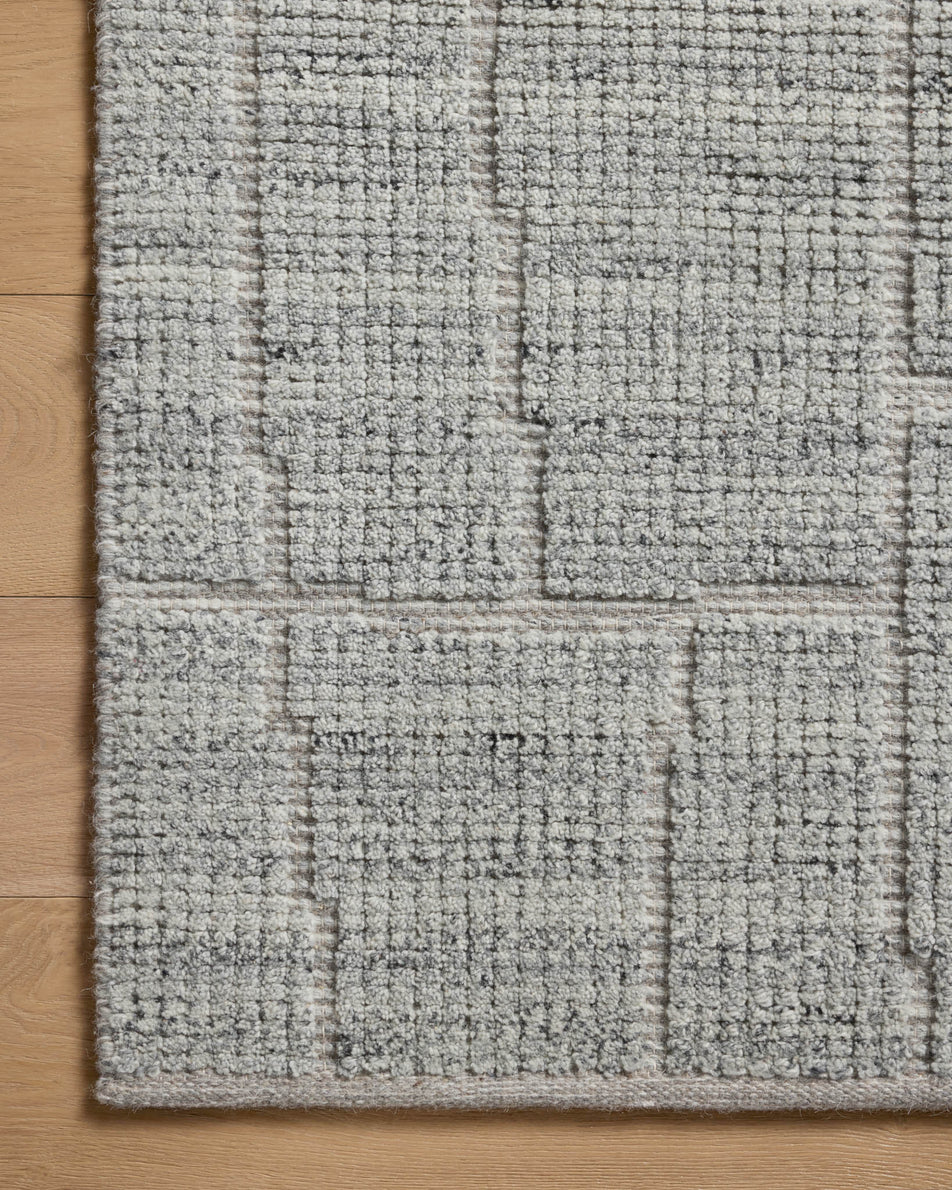 Close up of light gray textured area rug with raised geometric block pattern on hardwood floor, modern neutral rug detail