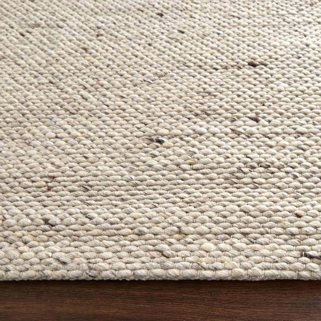 Close-up of natural wool jute braided area rug corner with chunky loop weave texture on wooden floor