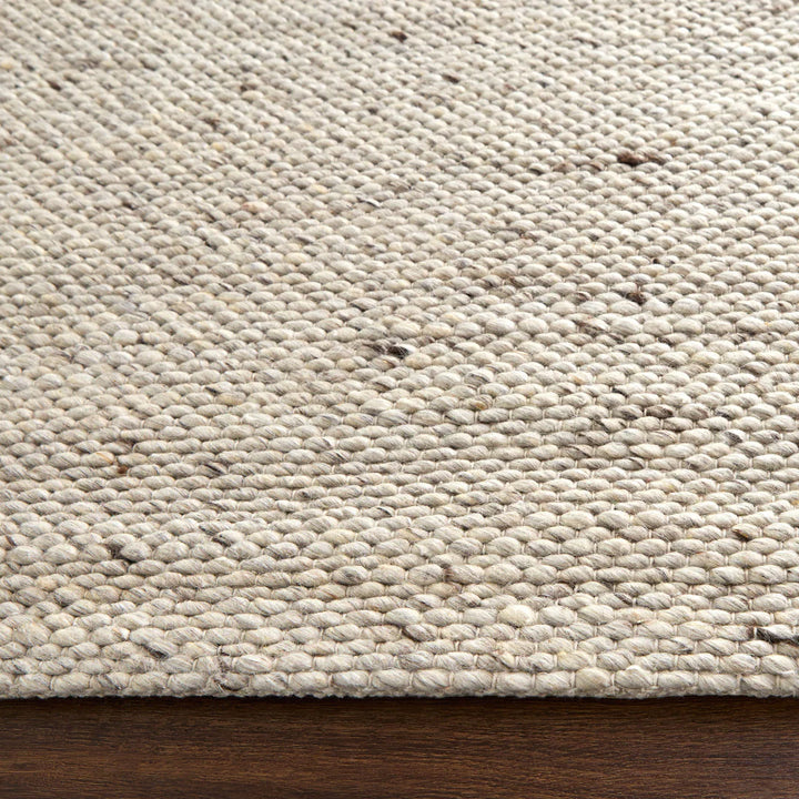 Close-up of natural wool jute braided area rug corner with chunky loop weave texture on wooden floor