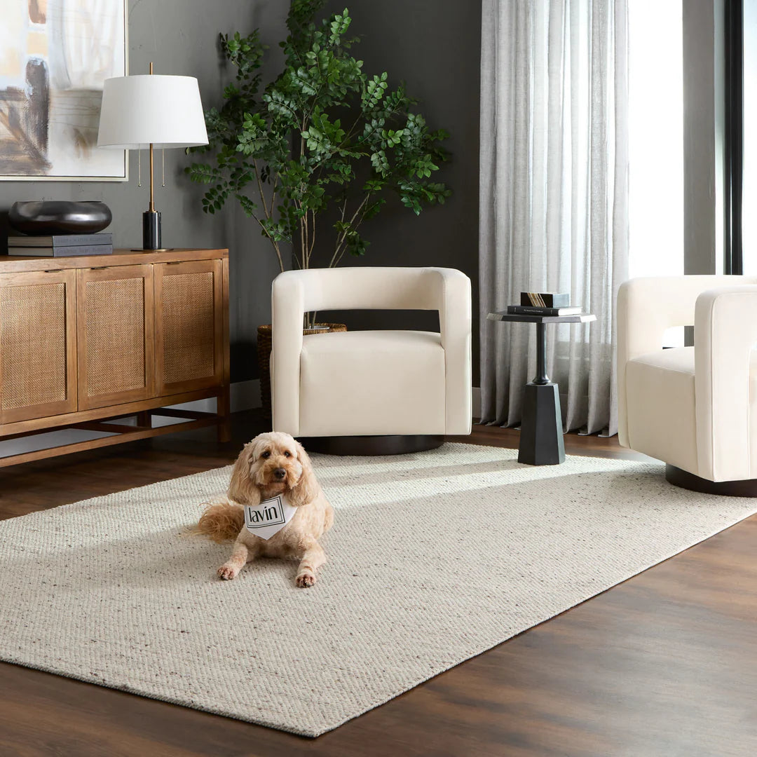 A beige wool blend rug with a monochromatic textural pattern, displayed in a room setting with furniture and a dog lying on it.