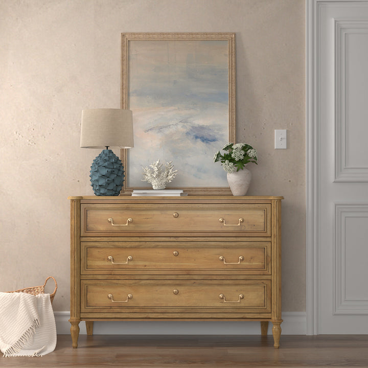 A wooden chest of drawers with brass hardware, placed against a wall in a room, with decorative items on top.