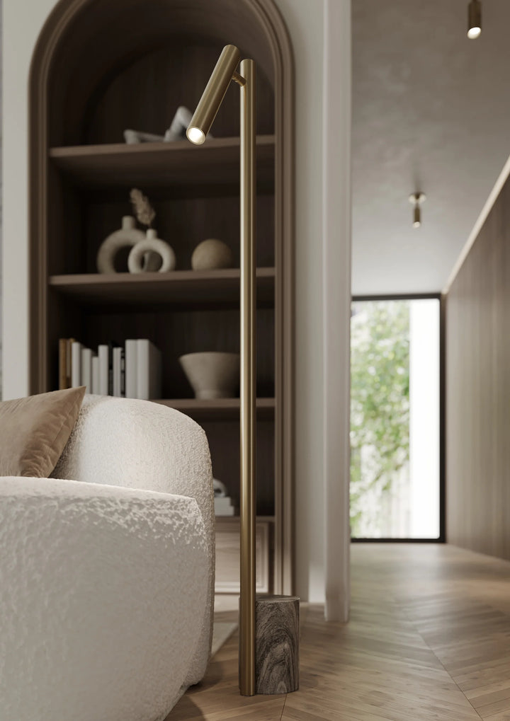A modern Circleville floor lamp with an articulating shade, featuring a brass finish, mounted in a contemporary interior setting with a bookshelf and lamp in the background.