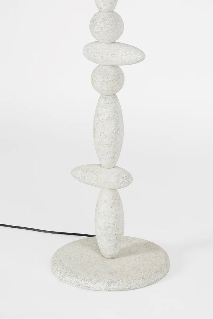 A modern Cullen Floor Lamp base composed of stacked, smooth, oval-shaped white stones with a speckled texture, inspired by Scottish dry stone design. A black electrical cord extends from the round base on a white background.