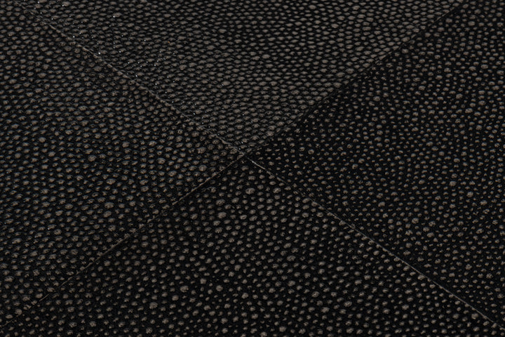 Black shagreen leather texture close-up with stitched panel seams forming a geometric cross pattern