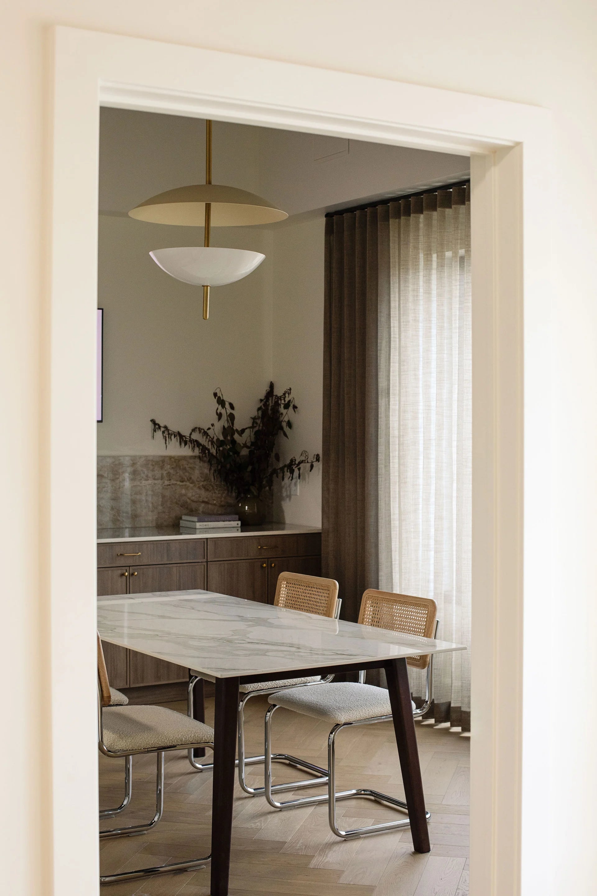 Dining room with marble table and chairs, featuring a modern light fixture.