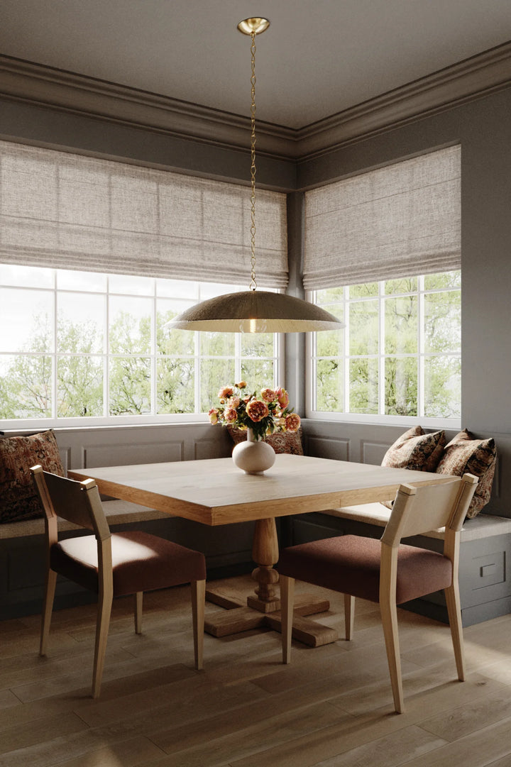 A modern pendant ceiling light with a sculptural dome shape, in a warm silver leaf finish, hanging over a wooden table with four chairs in a room with window treatments and decor.