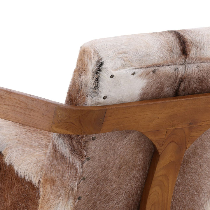 Close-up of cowhide accent chair showing natural fur texture, nailhead trim, and warm wood armrest detail