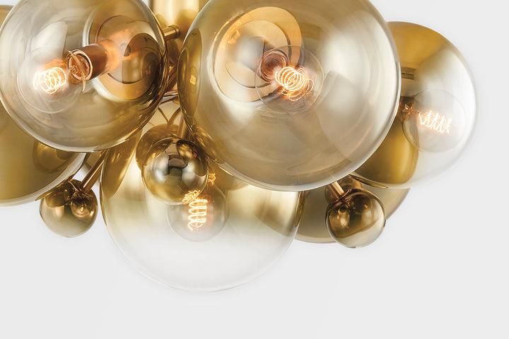 Close-up of modern brass chandelier with amber glass globe shades and exposed Edison filament bulbs glowing warm light