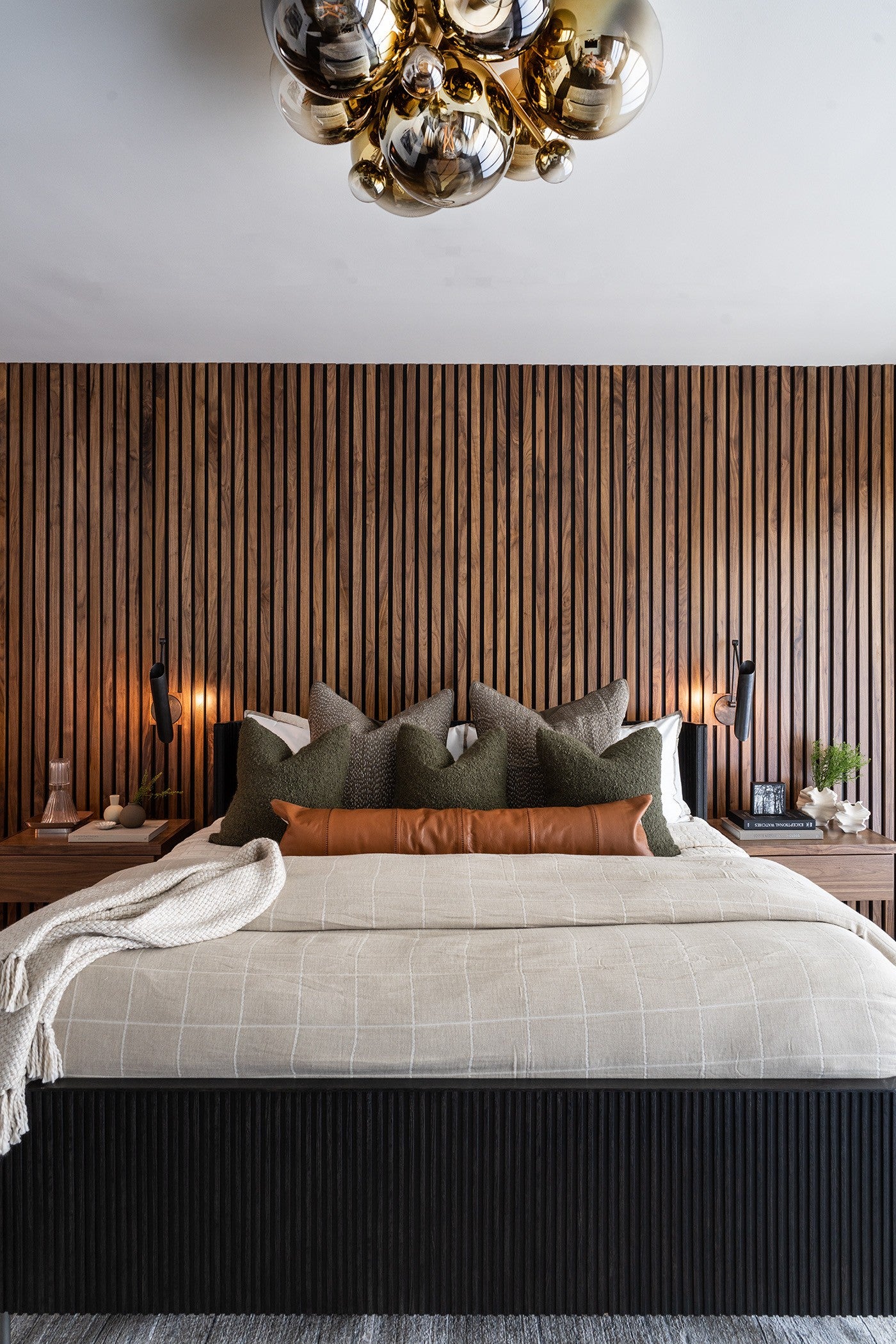 Clustered ombre glass globe ceiling light fixture in a room with wood accent wall and a bed with beige bedding.