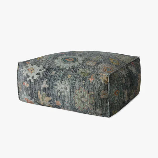 A multicolored square-shaped ottoman with a patterned fabric upholstery.