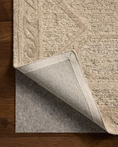 Close-up of a beige textured rug with a corner showing the carpet pad on a wooden floor.
