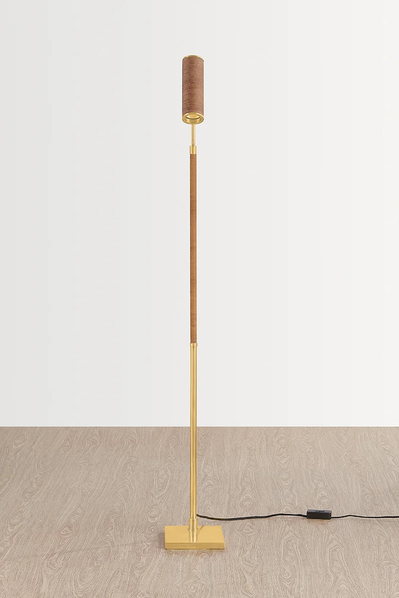 Slim brass floor lamp with square base and small cylindrical fabric shade on a light background
