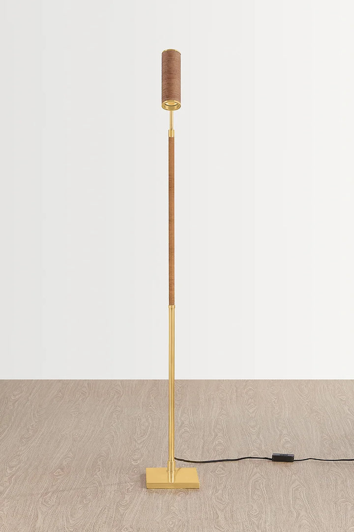 Slim brass floor lamp with square base and small cylindrical fabric shade on a light background
