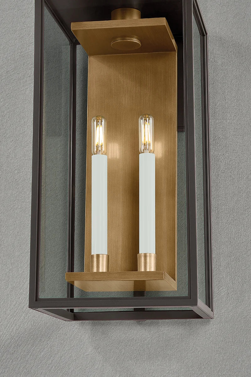 Close-up of modern black metal and brass outdoor wall lantern with clear glass panels and two candle-style bulbs