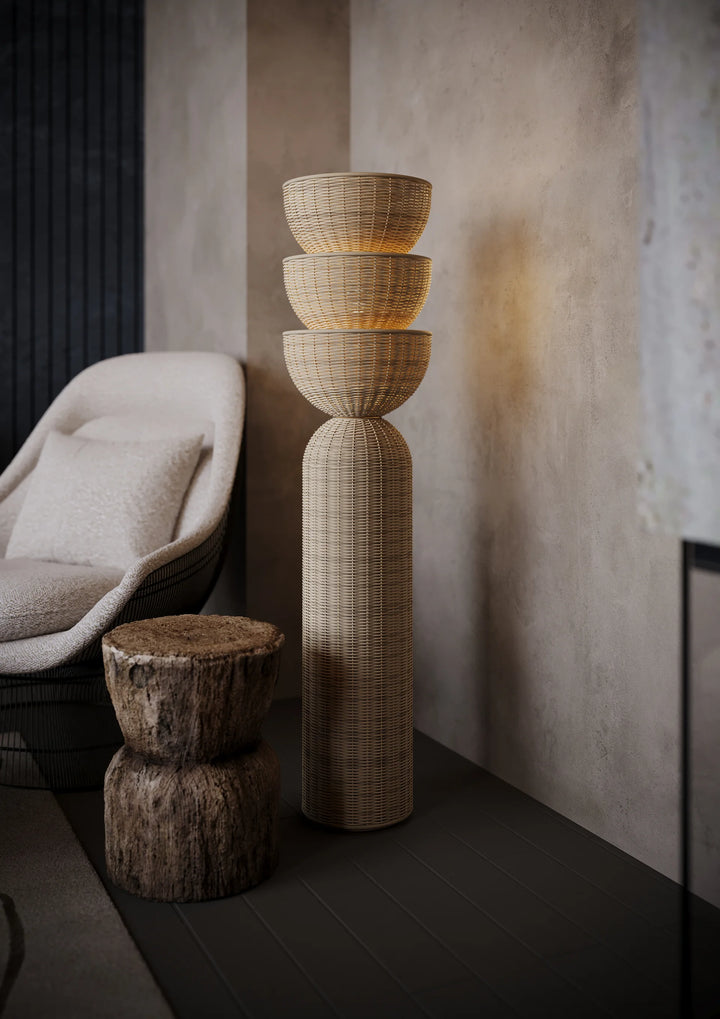 Tall woven rattan floor lamp with stacked basket shade in a modern neutral living room beside a boucle chair and wood stump side table