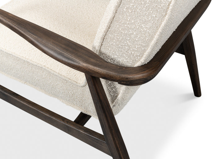 Close-up of cream upholstered accent chair with dark wood armrest and angled legs, showing textured fabric and modern frame details