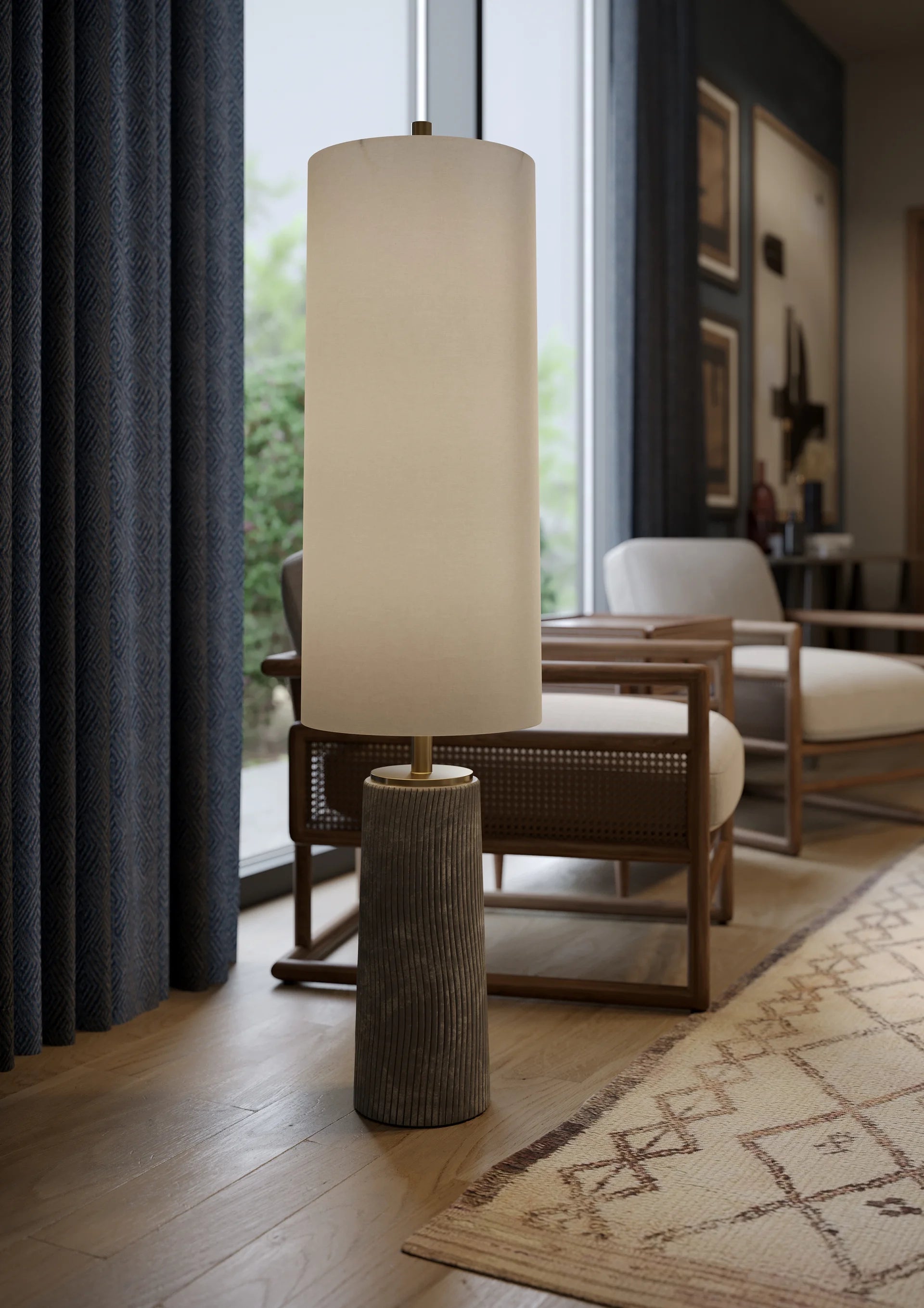 A modern floor lamp with a natural linen shade and a ceramic base featuring a raked, zen garden-inspired pattern, standing in a well-lit living room next to a chair with a wooden backrest.