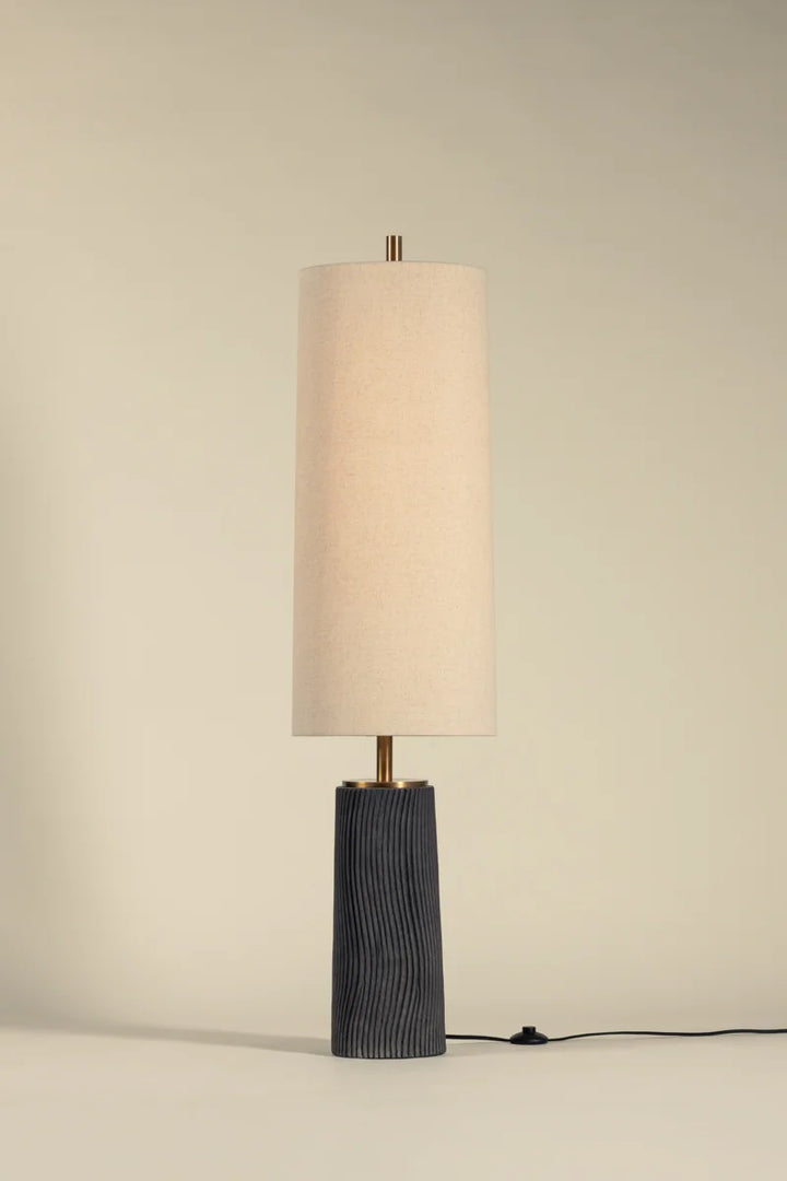 Modern table lamp with tall linen drum shade, dark ribbed base, and brass accent on neutral background with cord