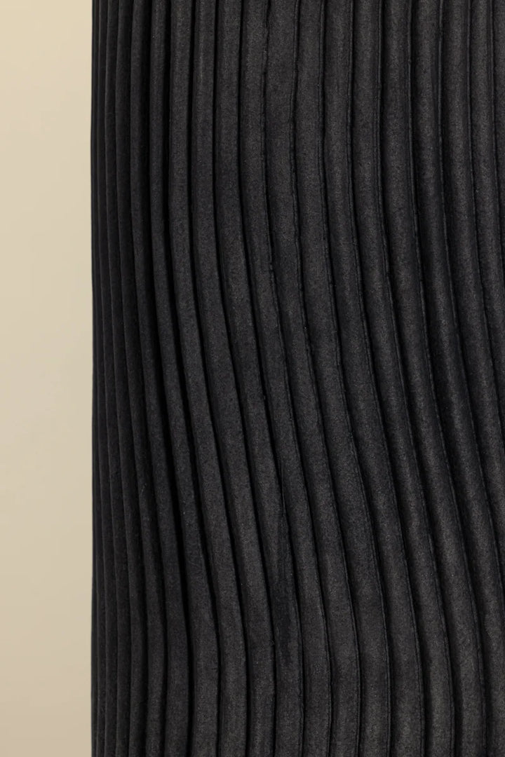 Close-up of charcoal ribbed ceramic table lamp base with wavy vertical texture on neutral background
