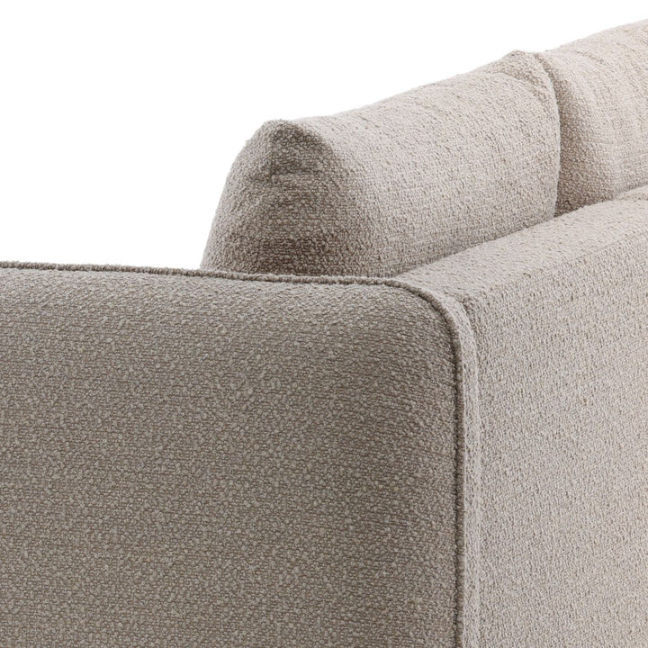 Close up of beige textured sofa upholstery showing wide armrest, piping detail, and plush back cushion