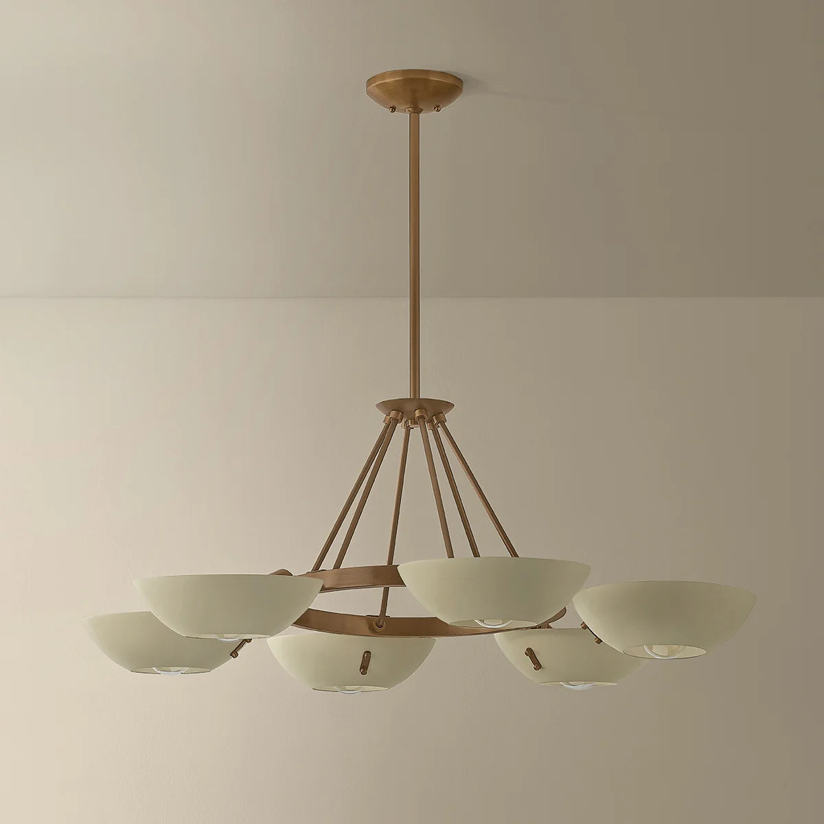Chandelier with gold frame and white shades on a beige wall