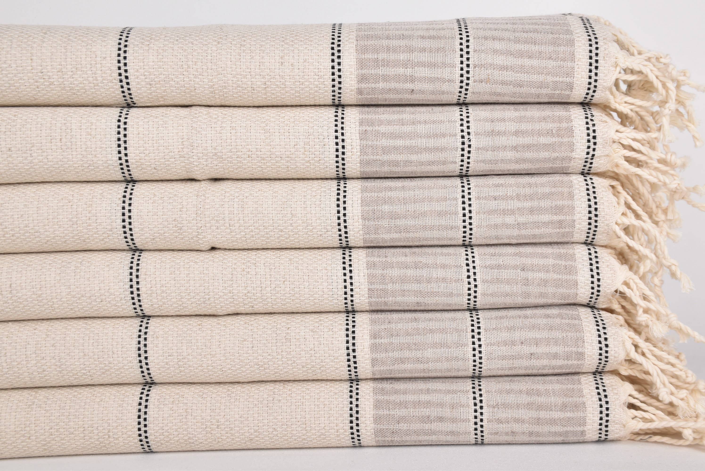 Stack of beige and gray striped towels with tassels on a light background