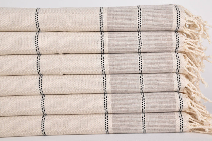 Stack of beige and gray striped towels with tassels on a light background