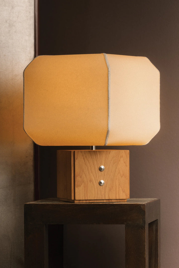 Modern table lamp with wooden base and split fabric shade on a dark surface.