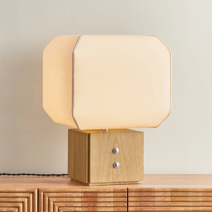 Table lamp with a wooden base and beige fabric shade on a wooden surface.