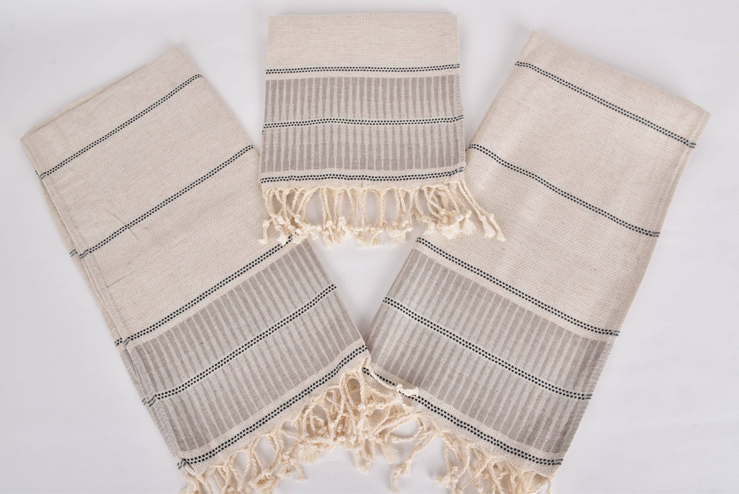 Set of three beige towels with black stripes and fringes on a light gray background