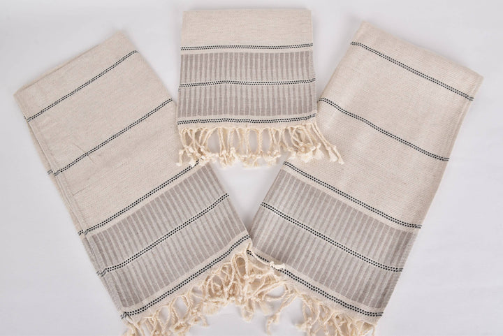 Set of three beige towels with black stripes and fringes on a light gray background