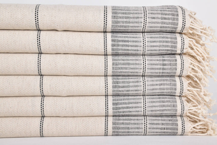 Stack of folded towels with striped pattern and fringes on a light background