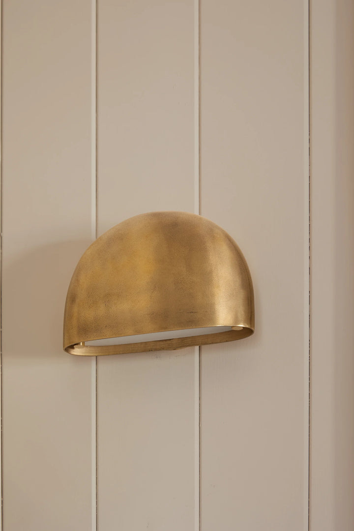 Gold wall-mounted light fixture on a beige paneled wall