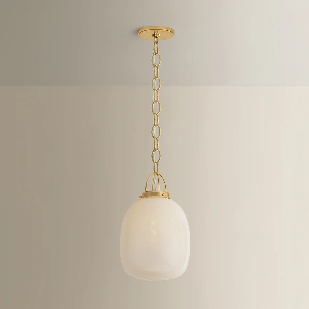 Pendant light with white glass shade and gold fixture on a neutral background