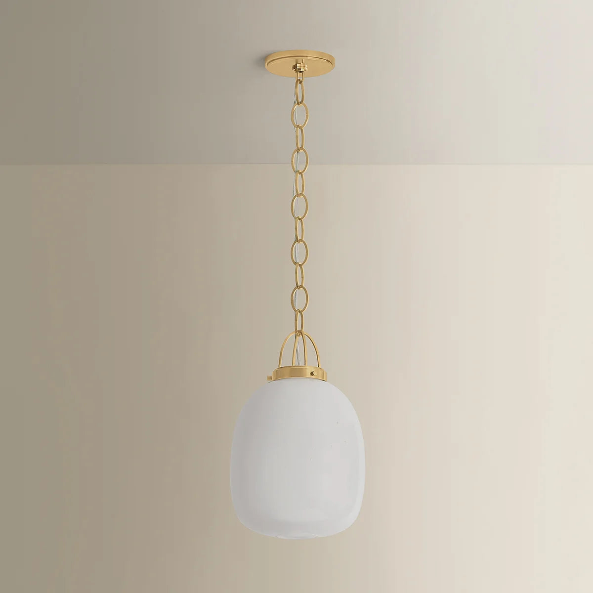 Pendant light with white glass shade and gold chain against a beige wall