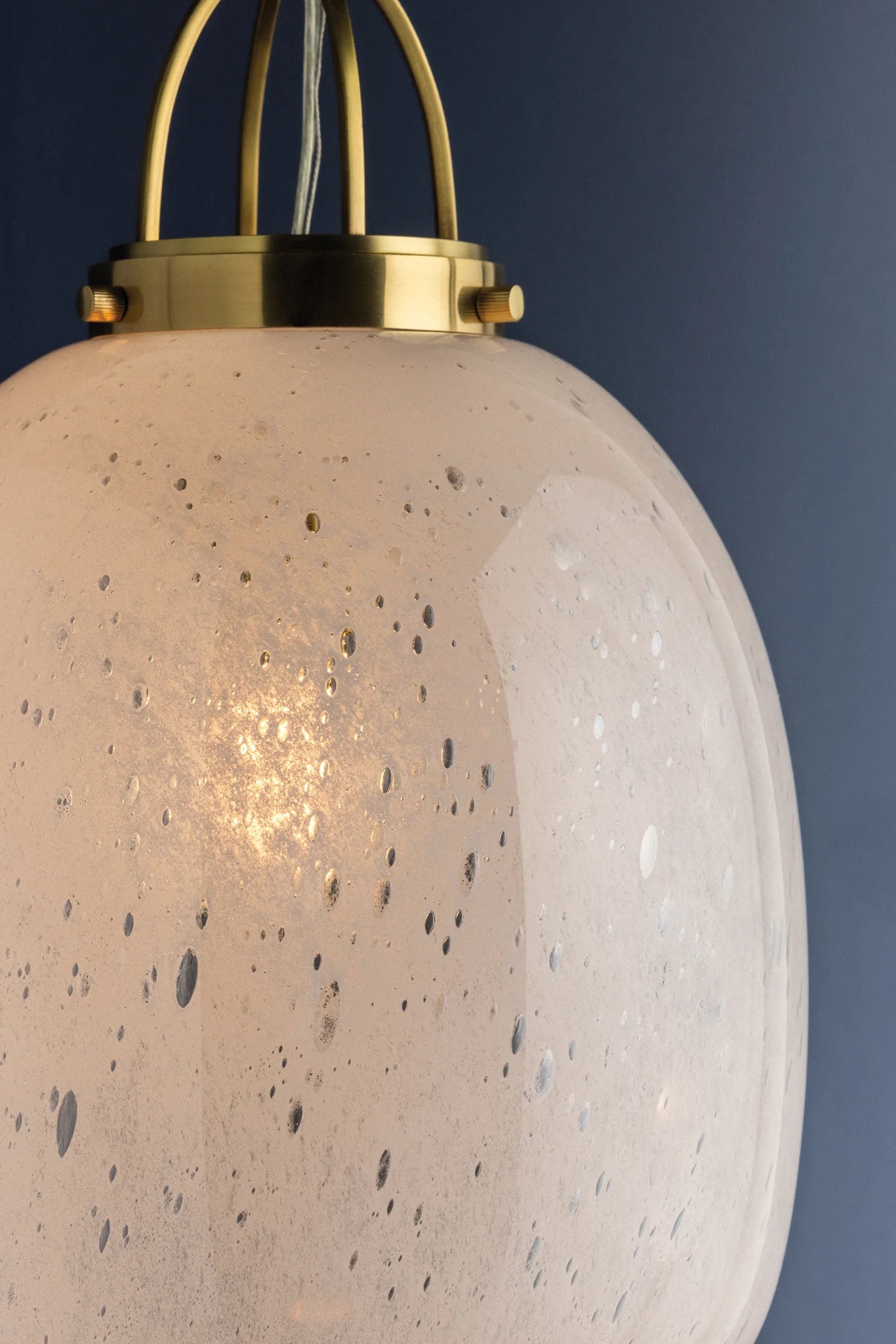 Close-up of a speckled glass pendant light with gold fixture against a dark background