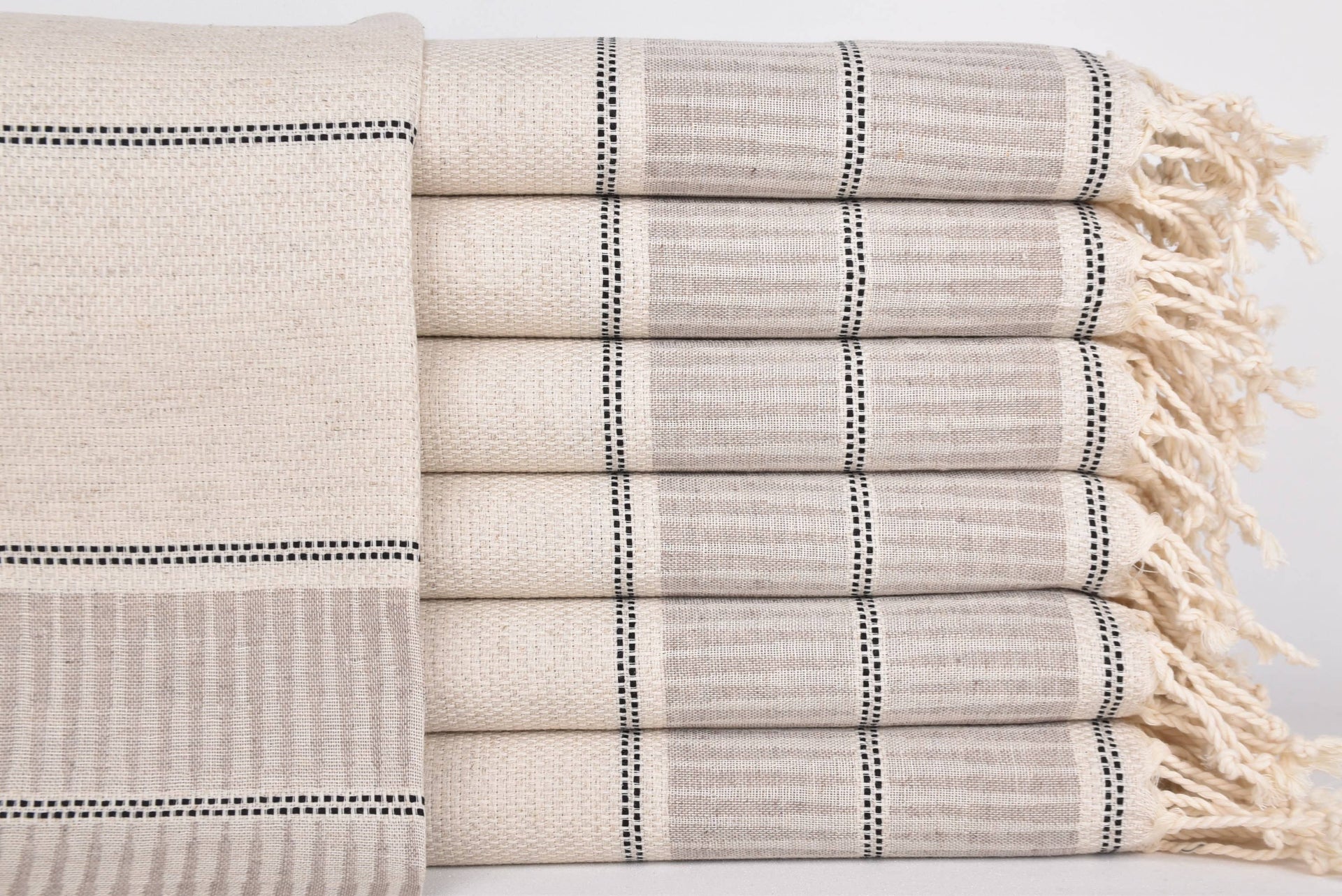 Stack of folded towels with striped pattern and tassels on a light background