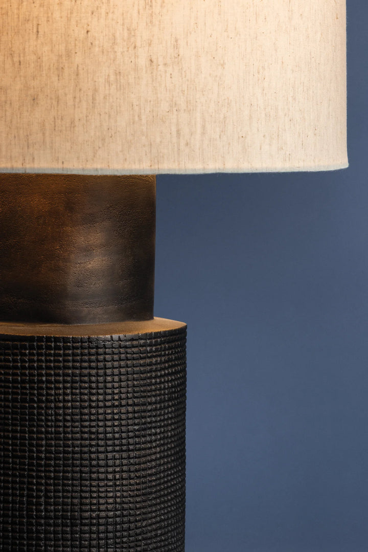 Close-up of a lamp with a textured black base and beige lampshade against a blue background