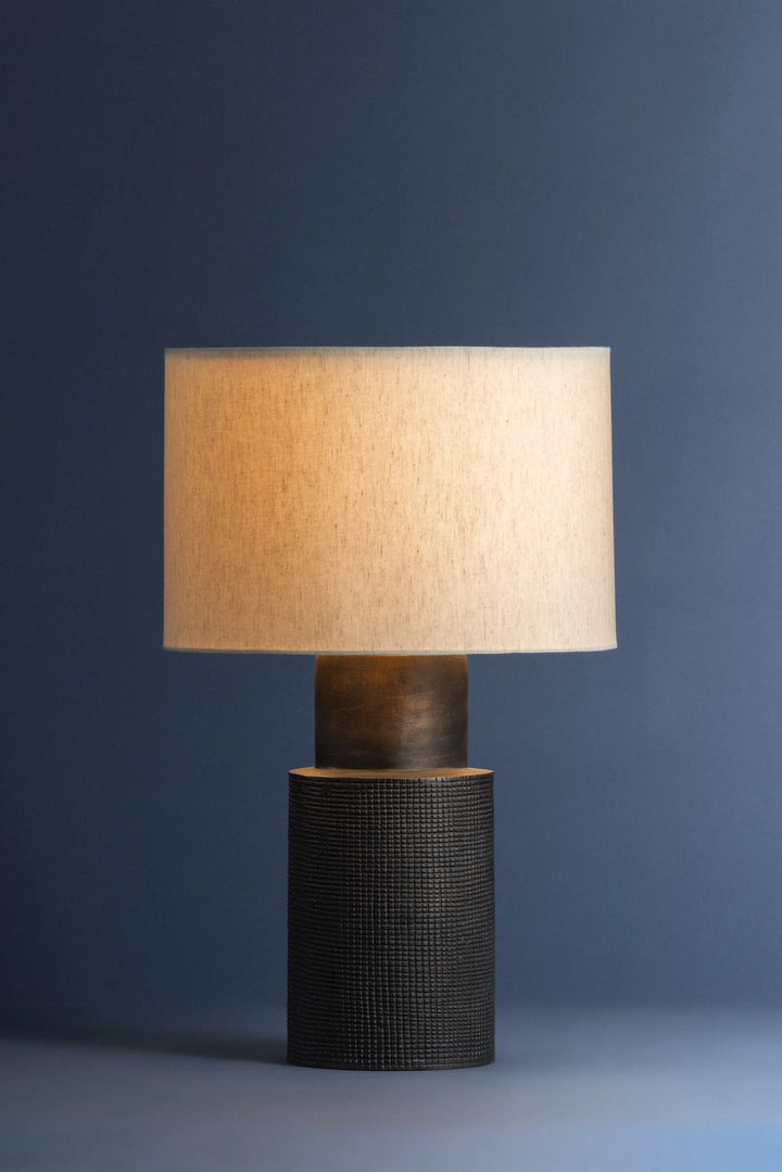 Table lamp with a textured base and beige lampshade against a dark blue background