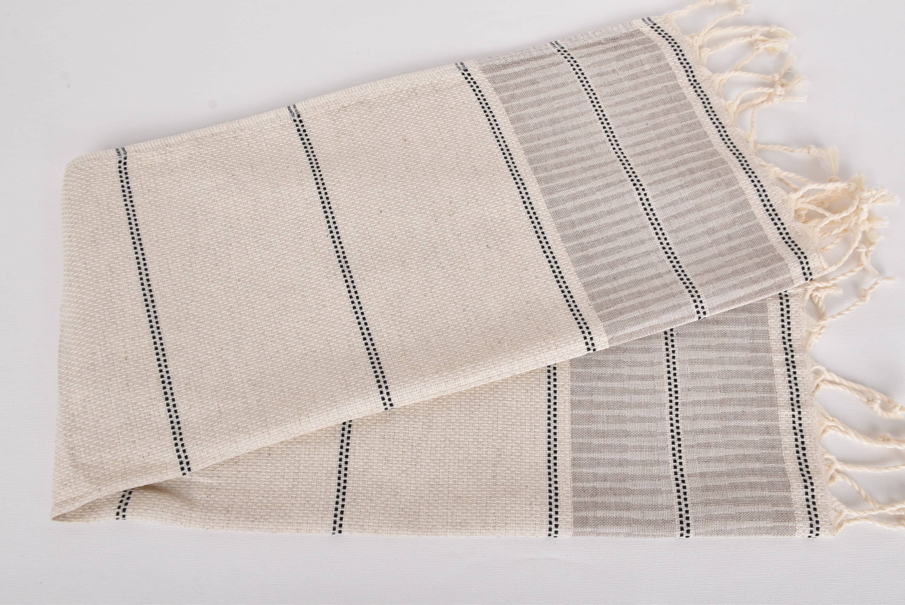 Beige towel with black stripes and white tassels on a light gray background