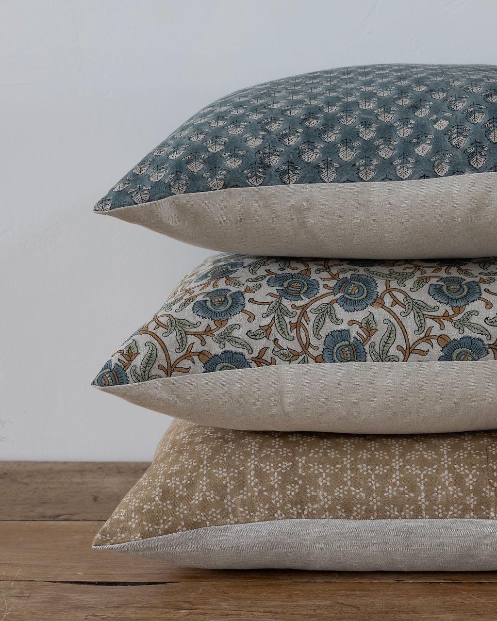 Stack of three patterned pillows on a wooden surface with a neutral background