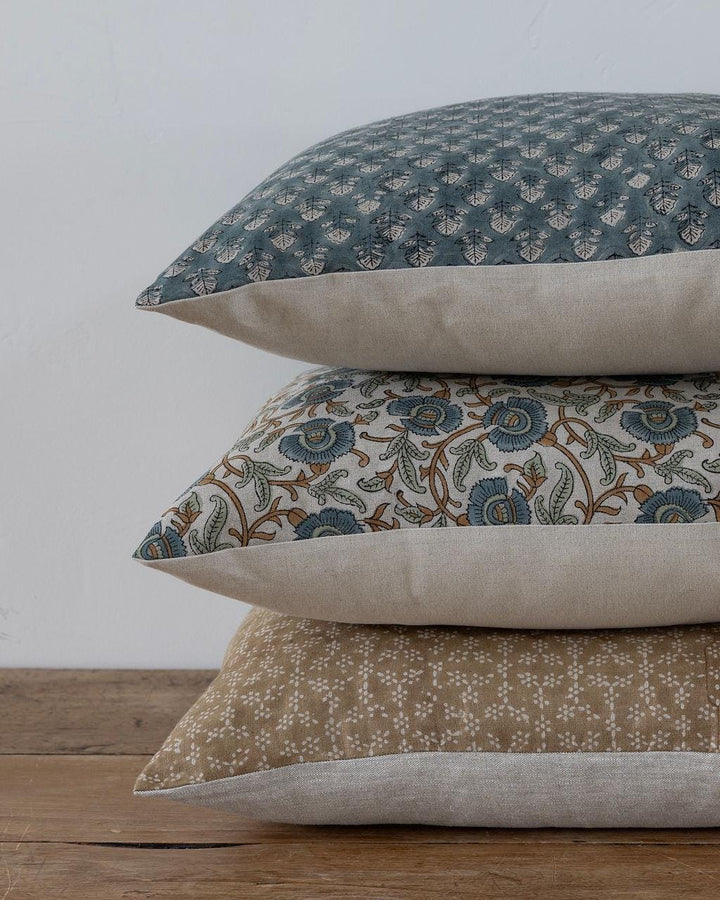 Stack of three patterned pillows on a wooden surface with a neutral background